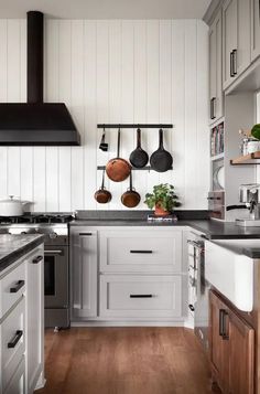 a kitchen with white walls and wooden floors has pots and pans hanging on the wall