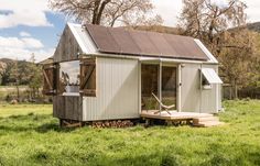 a tiny house with a porch and a deck in the middle of a grassy field