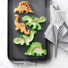 dinosaur cookies are on a baking tray next to a spatula and utensils