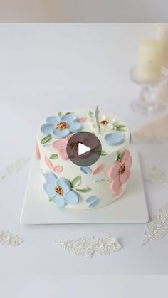 a white cake with flowers on it and a candle in the middle, sitting on a table