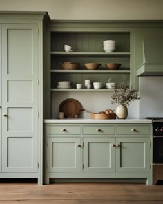 a kitchen with green cupboards and white counter tops, wooden floors and open shelves