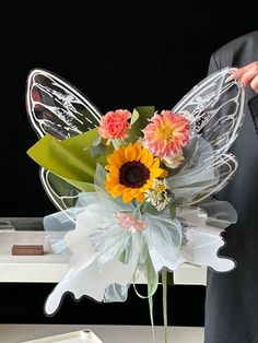 a man holding a bouquet of flowers in front of a butterfly shaped vase with wings