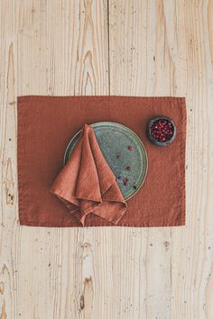 a place mat with a red napkin and a bowl of berries next to it on top of a wooden table