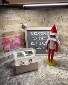 a sign that says welcome to the elf era tour next to a small toy doll