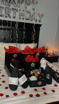 a bed topped with lots of black boxes filled with shoes and presents next to a happy birthday sign