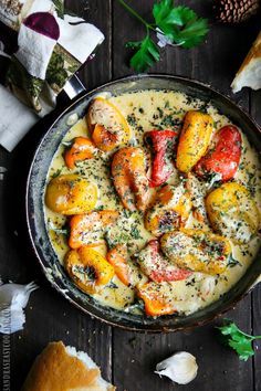 a pan filled with potatoes and meat on top of a wooden table next to bread