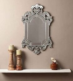 a mirror and candles on a shelf in front of a wall with an ornate frame