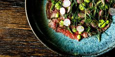 a blue plate topped with meat and veggies on top of a wooden table