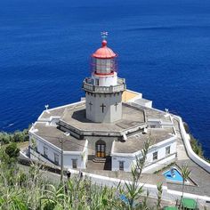 a light house sitting on top of a hill next to the ocean in front of blue water