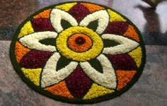 a circular design made out of flowers on top of a marble flooring area with red, yellow and white colors