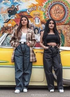 two women standing in front of a yellow car