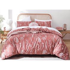 a bed with pink comforter and pillows on top of it in a room next to a table