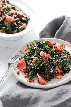 a white plate topped with greens next to a bowl filled with meat and vegetables on top of a table