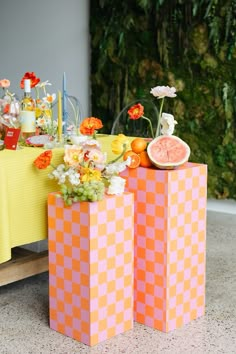 two orange and pink boxes with flowers in them next to a yellow table cloth covered table