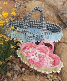 two purses are sitting on the ground next to some flowers and rocks, one is made from fabric