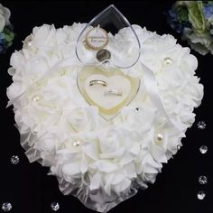 a heart shaped box filled with white flowers and two wedding rings on top of it