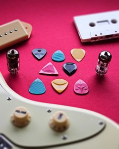 several guitar picks are arranged on a pink surface next to an electric guitar and some other accessories