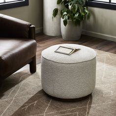 a white ottoman sitting on top of a wooden floor next to a chair and potted plant