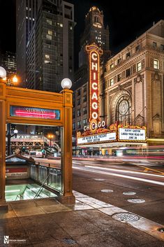 a city street at night with lights and buildings in the background, including an old theater marquee