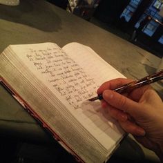 a person holding a pen and writing on an open book with the pages lined in cursive writing