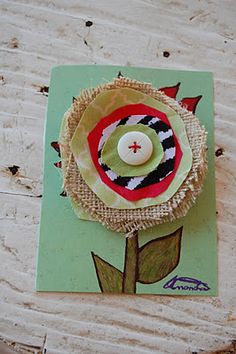 a flower made out of burlap on top of a piece of paper with a button in the center