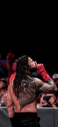 a man with long hair and tattoos on his chest standing in front of a crowd