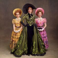 three women in long dresses and hats posing for a photo with their hands on their hips