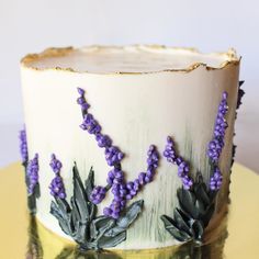 there is a cake with purple flowers on the frosting and gold plated surface