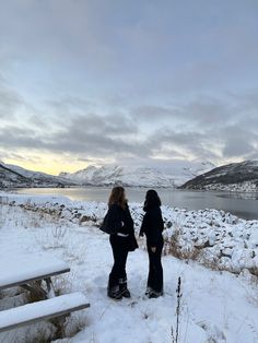 two women standing in the snow next to a lake