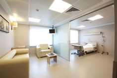 an empty hospital room with white walls and furniture in the foreground, there is a bed on the other side of the room