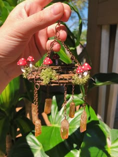 a person holding up a miniature house with mushrooms on the roof and chains hanging from it's sides