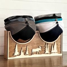 three hats are sitting on top of a wooden holder with moose and pine trees in the background