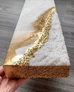 a hand holding a piece of cake with white and gold frosting