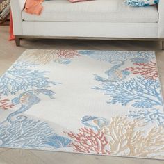 a white couch sitting next to a rug on top of a hard wood floor covered in colorful corals