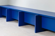 a blue bench sitting on top of a hard wood floor next to a white wall