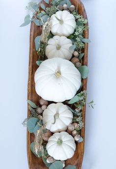 a wooden boat filled with white pumpkins and greenery