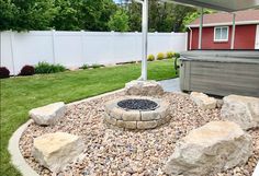 a fire pit surrounded by rocks and gravel in front of a white fenced backyard