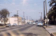 cars are driving down the street in front of buildings and palm trees on either side