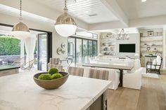 a large open concept kitchen and dining room with white marble countertops, stainless steel pendant lights, and modern lighting fixtures