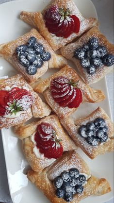 small pastries with berries and powdered sugar are arranged on a white platter