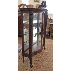 a wooden display case with glass doors and carvings on the top, in front of a carpeted area