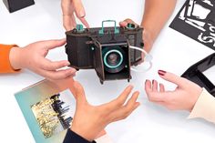 three people holding an old camera over a table