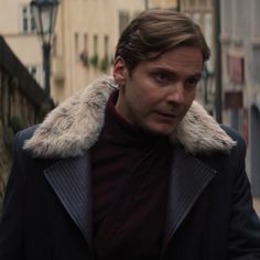 a man in a coat and fur collar walking down the street with his hand on his hip