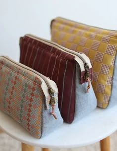 three purses sitting on top of a white table next to each other with zippered closures