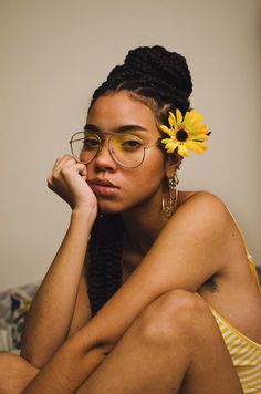 a woman with glasses and a flower in her hair sitting on a bed looking at the camera