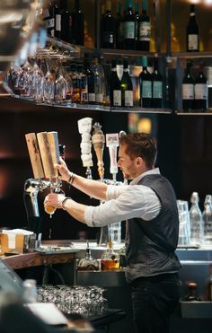 a man is making a drink at a bar with lots of bottles on the shelves