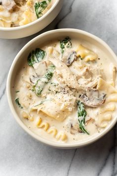 two bowls filled with pasta and spinach on top of a marble countertop next to each other