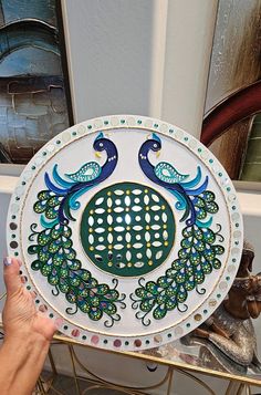 a hand holding a decorative plate with peacocks on it