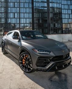 a grey lamb suv parked in front of a building with large windows and orange rims