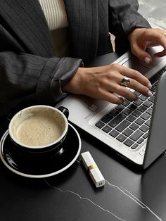 a woman using a laptop computer while sitting at a table with a cup of coffee